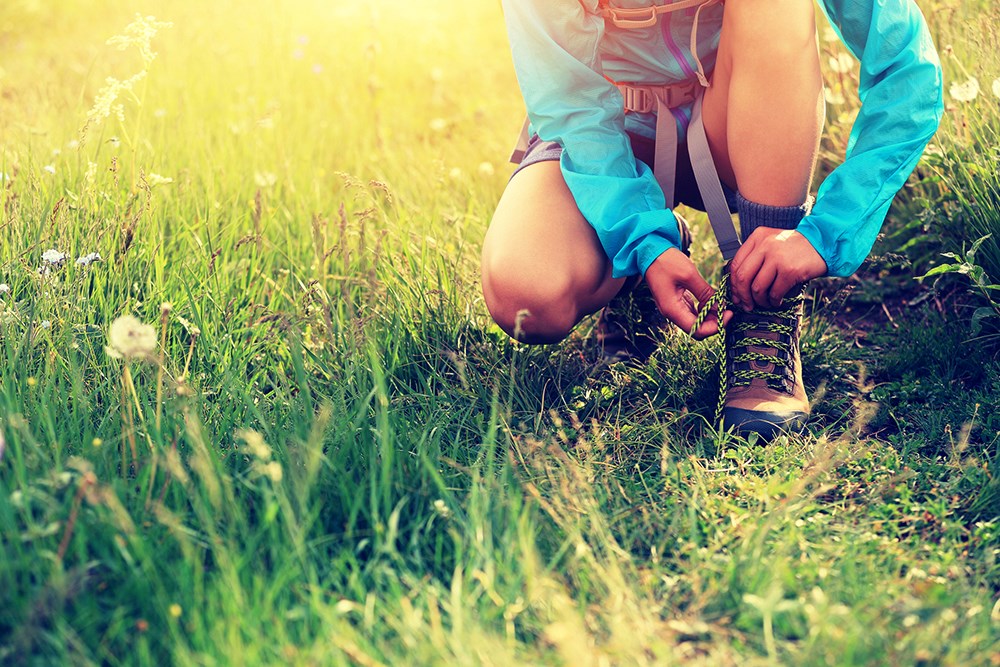 woman hiker tying shoelace on grassland grass