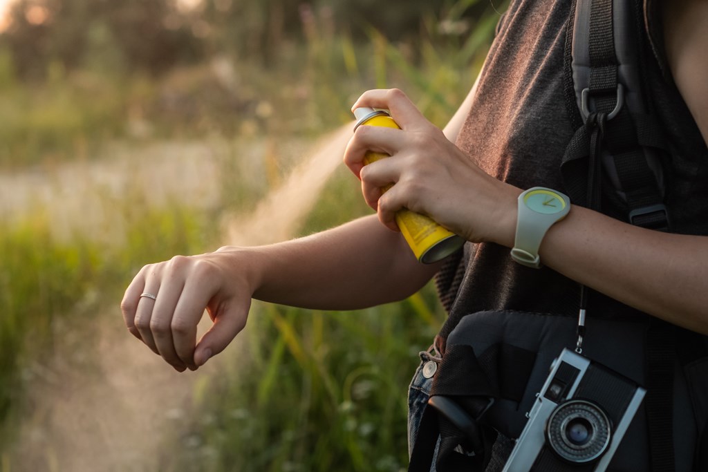 Close-up of young female backpacker applying bug spray on hands.