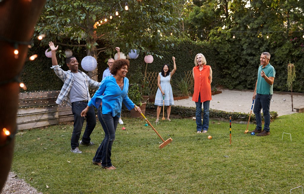 Group of older friends of different ethnicities playing croquet in the backyard.