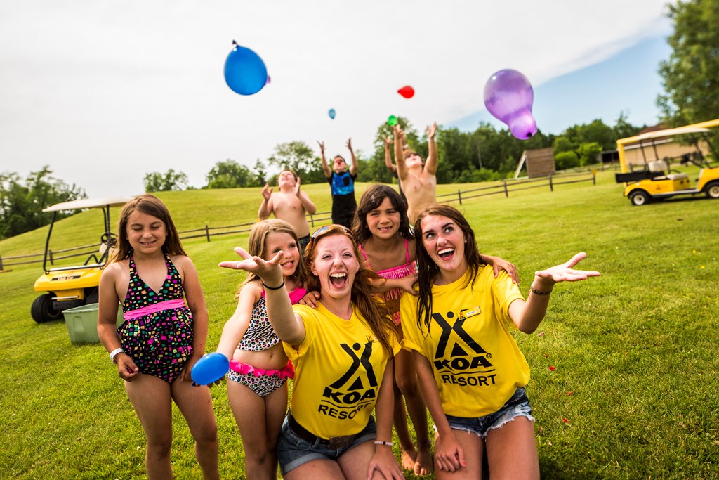 Two KOA employees in yellow shirts throw water balloons in the air with young campers.