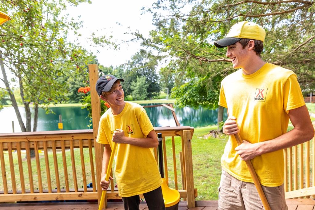 Two high school-age KOA campground employees in yellow shirts laugh as they work.