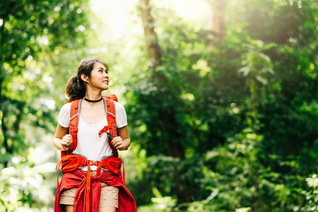 Young woman looks at the trees around her as she hikes in a forest.