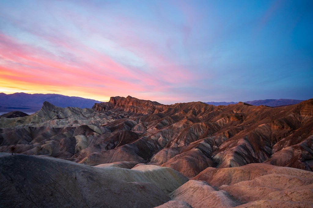 Pink sunset over Zabriskie Point in Death Valley National Park - a unique hilly area with visible sedimentary layers.