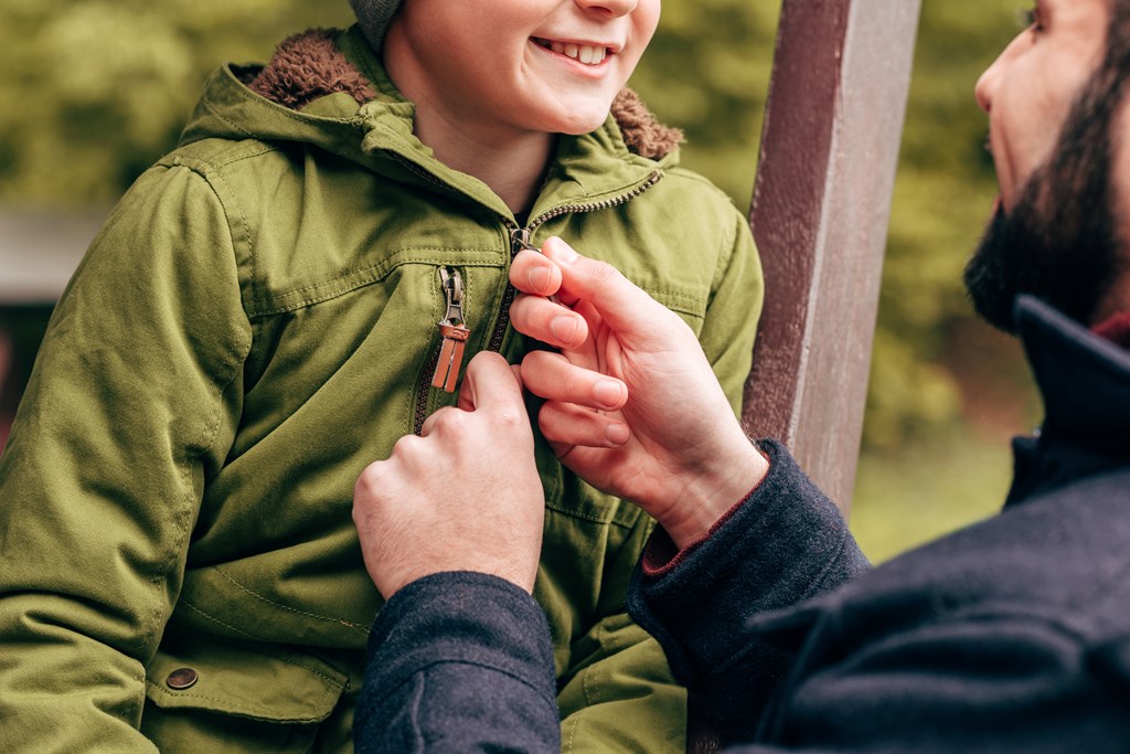 Close up of father fastening jacket of young son while camping.