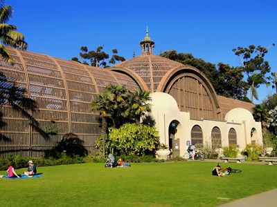 People sitting on a large grassy area in front of the Botanical Building in Balboa Park.