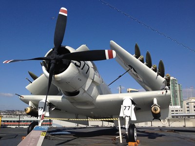 Large white aircraft with a red and black propellor sitting atop the Midway Aircraft Carrier.