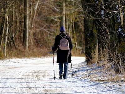 Woman wearing a black coat and purple beanie goes hiking on a rocky and snow covered trail.