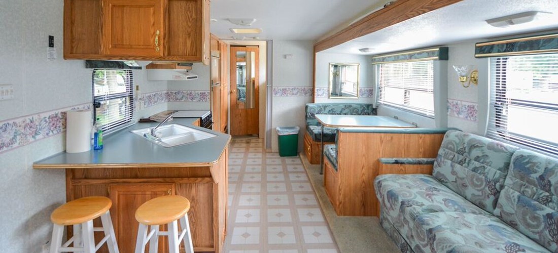 Inside a travel trailer: pull-out sofa in forefront, door to bathroom in back ground