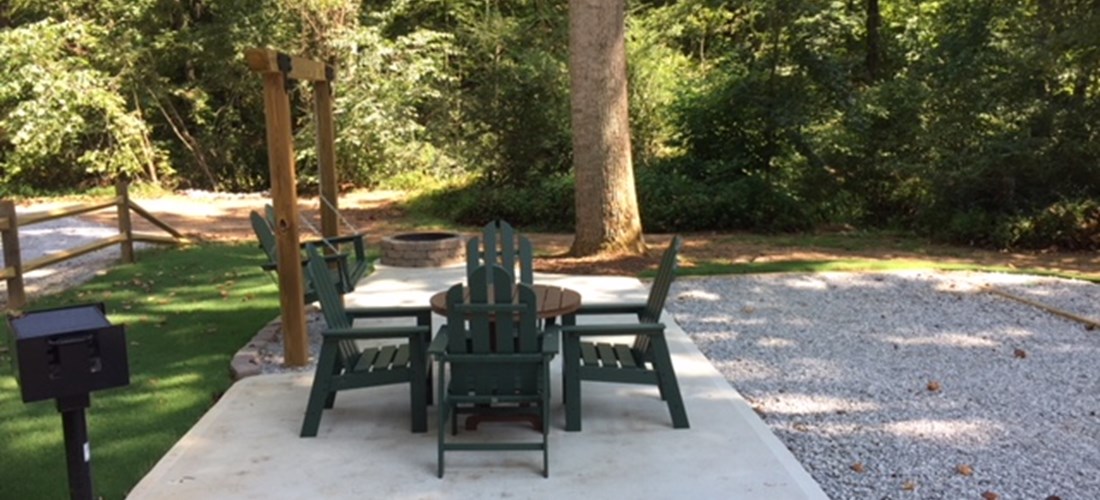 KOA Patio Site in our New Section in the back of the park. Concrete patio, table and chairs, swing, charcoal grill and fire pit.