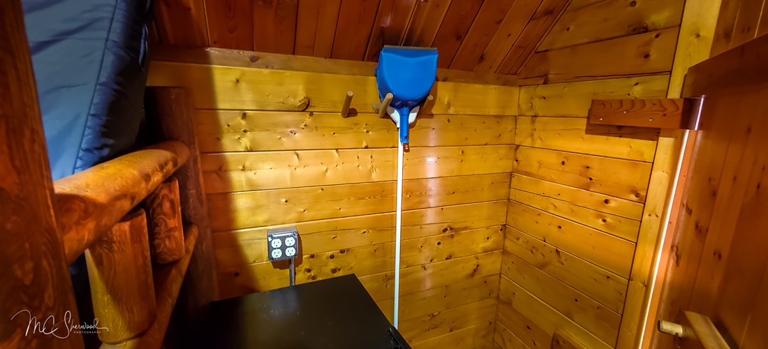 One-room rustic camping cabin interior - dorm fridge and broom