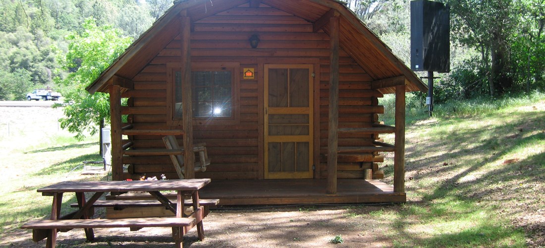 Our 2 room rustic cabins with added amenities have water on site, electricity inside the cabin, as well as a ceiling fan and heater. These cabins also include a mini fridge, microwave, air conditioning, tv with dvd or bluray combo, and HD cable tv. This cabin features a double sized bed in one room, a double sized bed and a bunk bed in the other room. You bring your bedding. All cabins have wifi access along with a picnic table and bbq grill. Pictured is cabin 108.