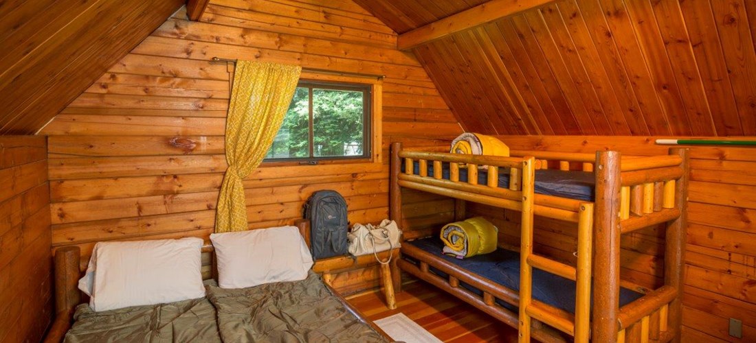 Inside of our camping cabins(linens/sleeping bags not included). A full size bed and a set up twin bunk beds, TV with cable. A fire ring, picnic table and parking for 1 vehicle at each cabin site.