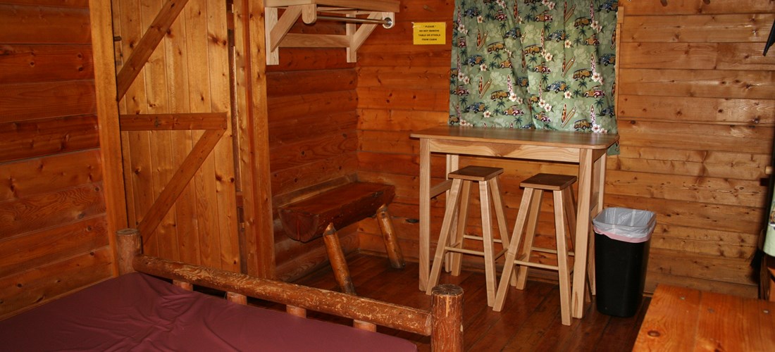 Inside a Two Room Cabin, front room with a full size bed and small table.