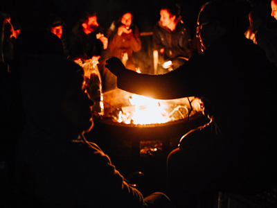 Campers gathered around a glowing campfire at night at Valdez KOA Journey.